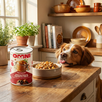 Dog looking at a bowl of food next to a can of Omni pet food on a wooden kitchen counter.