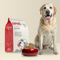 Dog sitting next to a bag of Omni pet food and a bowl of kibble on a beige background